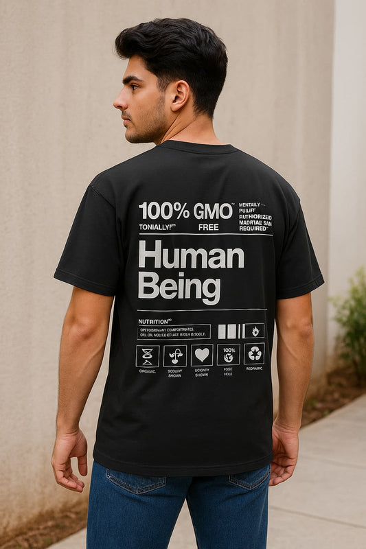 Person wearing a black t-shirt with text on the back, standing against a beige wall.