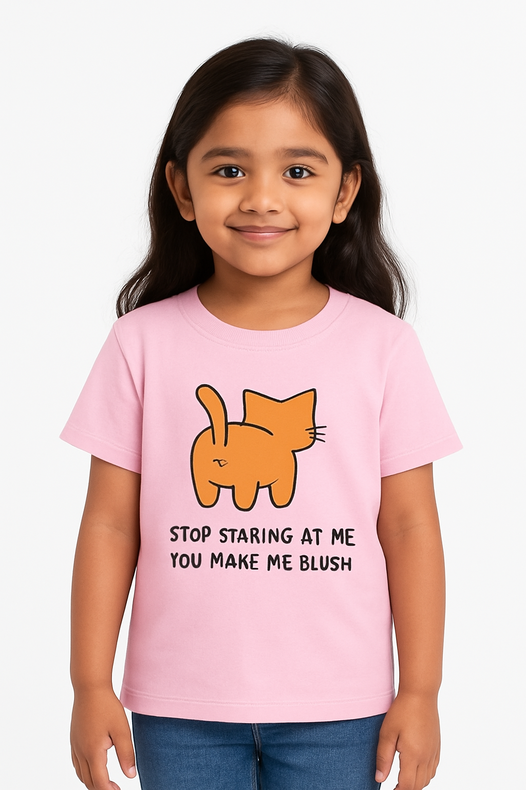 A young Indian girl with long dark hair smiles warmly while wearing a pastel pink T-shirt featuring a cartoon orange cat from behind and the text “STOP STARING AT ME YOU MAKE ME BLUSH.” She stands against a plain white background, creating a clean and kid-friendly e-commerce look.