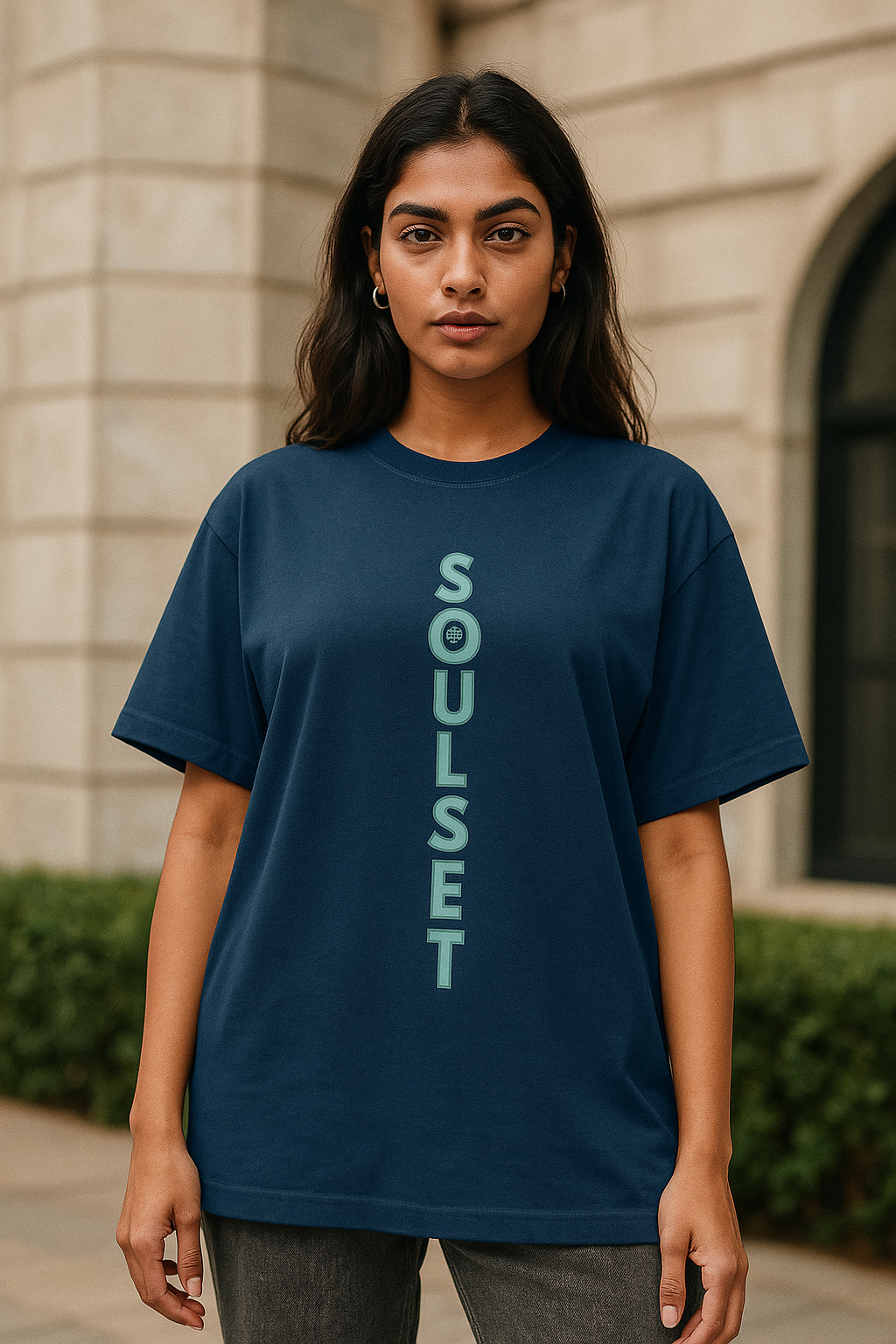 A confident and stylish Indian female model with a fair complexion and a fit build is wearing a navy blue oversized SoulSet t-shirt. The t-shirt features a bold vertical "SOULSET" text design printed in mint green on the front. The model is facing the camera in a relaxed pose, showcasing the front design clearly. The background is modern and minimal, keeping the focus on the t-shirt.