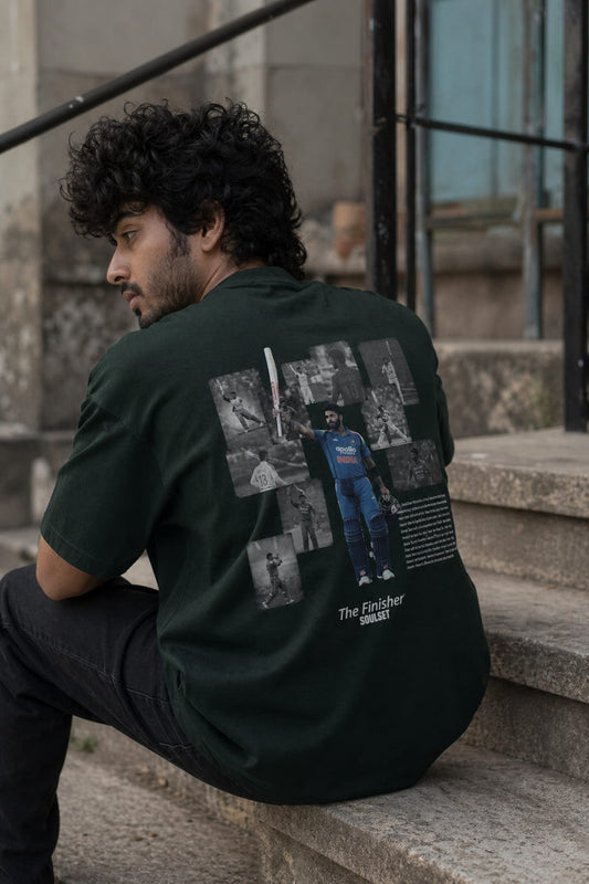 Man sitting on steps wearing a dark green t-shirt with graphic designs and text.