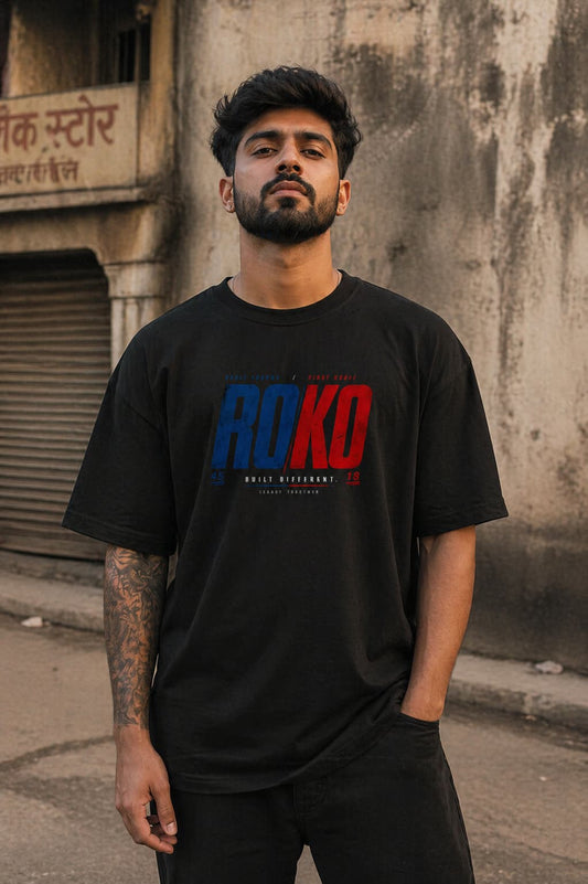 Man wearing a black t-shirt with 'ROKO' printed on it, standing against a textured wall.