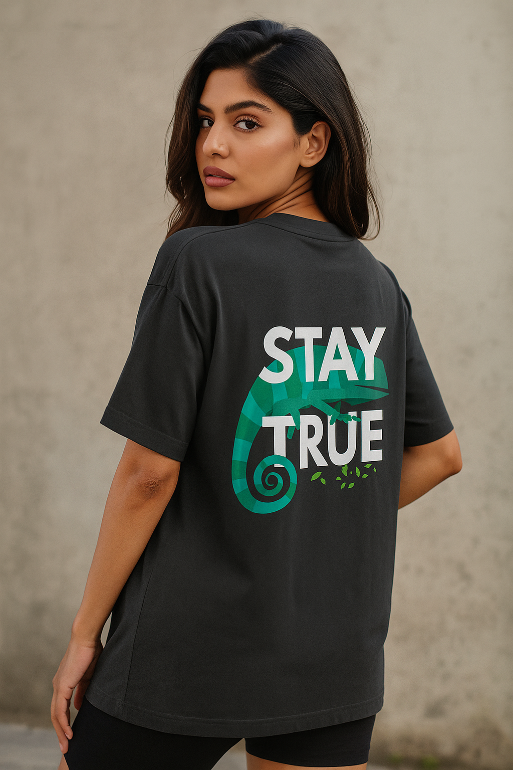 Indian female model in black oversized T-shirt showing back design with green chameleon and “Stay True” text – bold streetwear fashion.