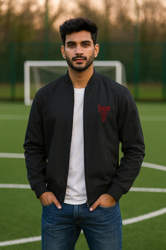 Man wearing a black bomber jacket with a red logo on a sports field