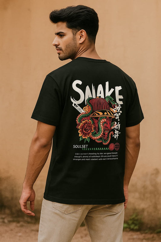 Man wearing a black t-shirt with a colorful graphic and text on the back, standing against a beige wall.