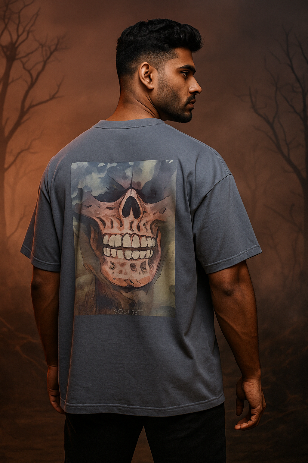 Man wearing a blue t-shirt with a skull design on the back against a dark, forest-like background.