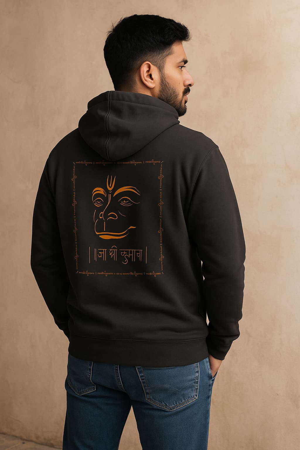 Person wearing a black hoodie with a face design and text on the back against a beige background