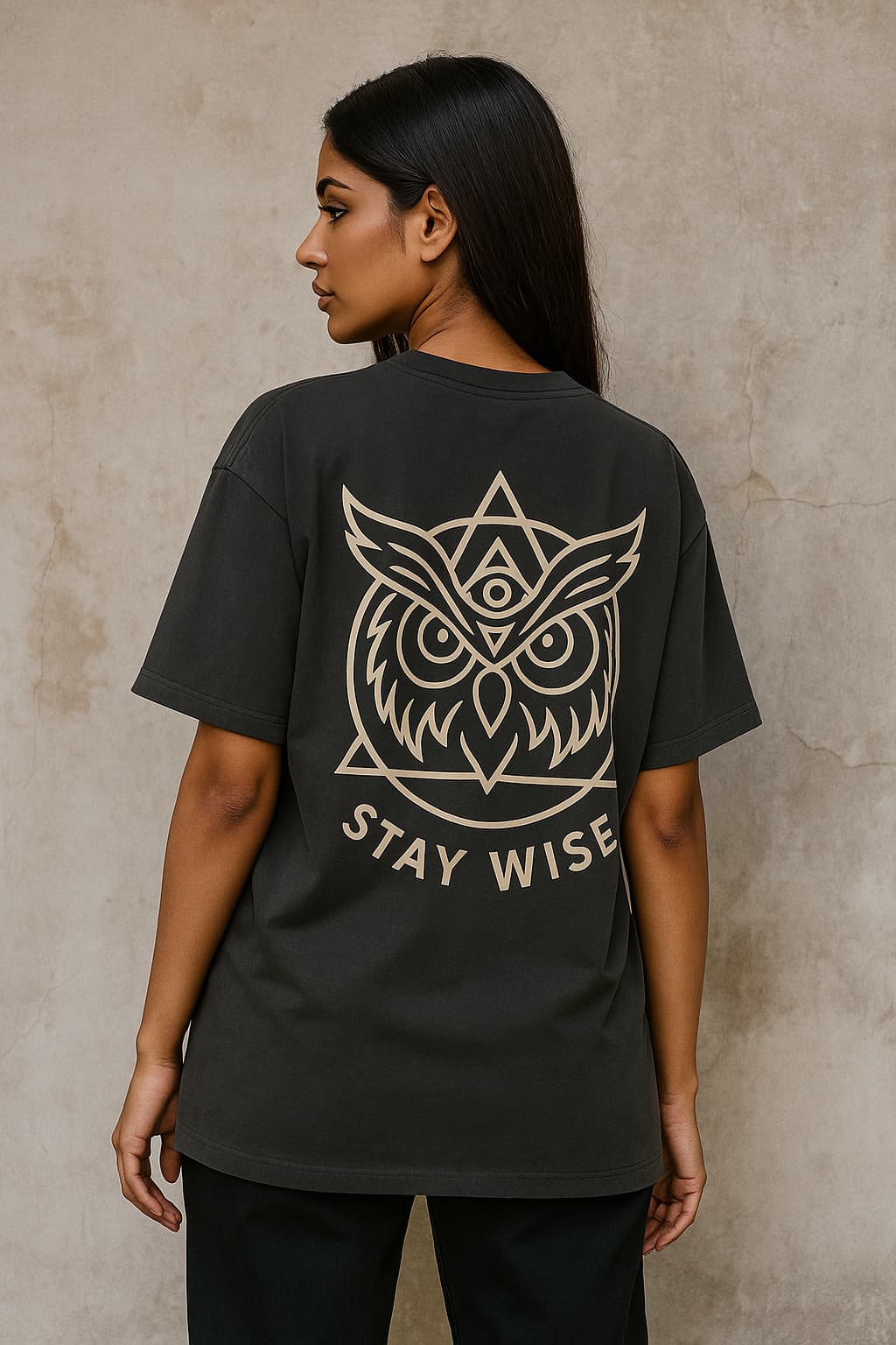 Person wearing a black t-shirt with an owl design and 'Stay Wise' text on the back against a beige wall.