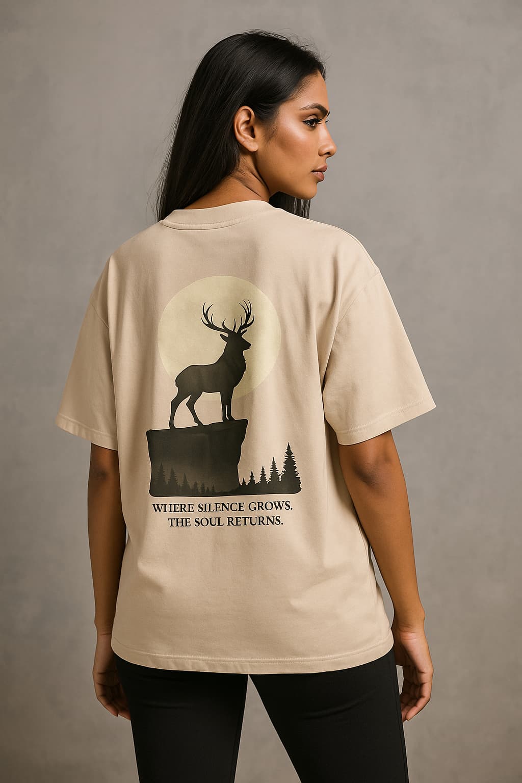 Woman wearing a beige t-shirt with a deer graphic and text on the back against a gray background
