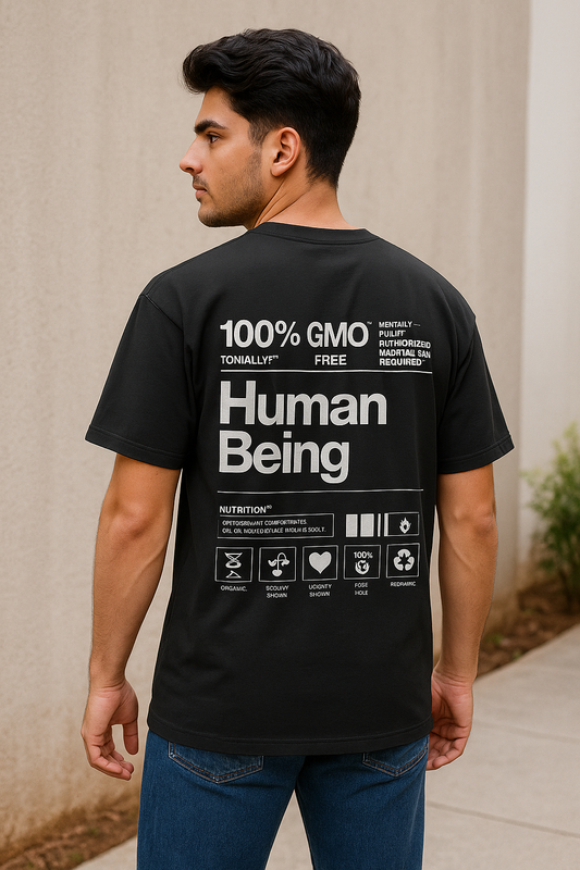 Man wearing a black t-shirt with text on the back, standing against a beige wall.