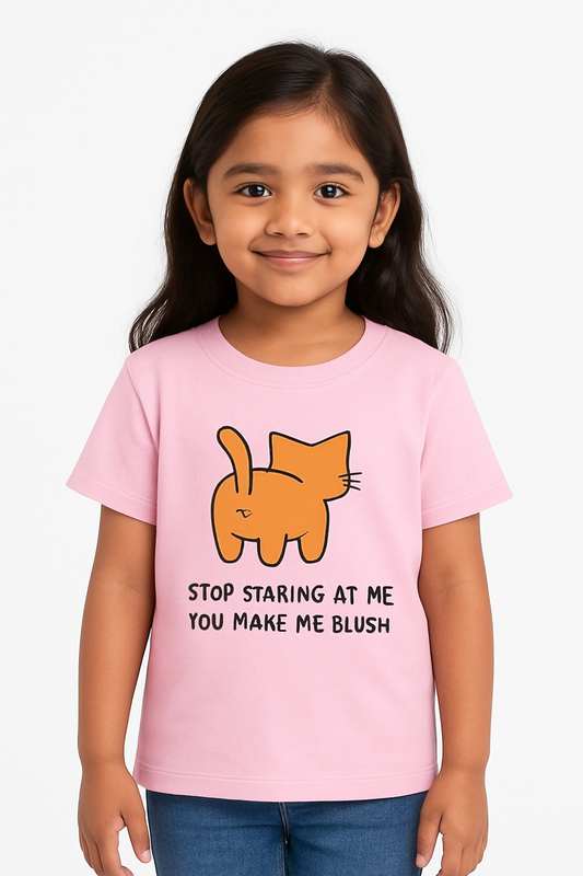 A young Indian girl with long dark hair smiles warmly while wearing a pastel pink T-shirt featuring a cartoon orange cat from behind and the text “STOP STARING AT ME YOU MAKE ME BLUSH.” She stands against a plain white background, creating a clean and kid-friendly e-commerce look.