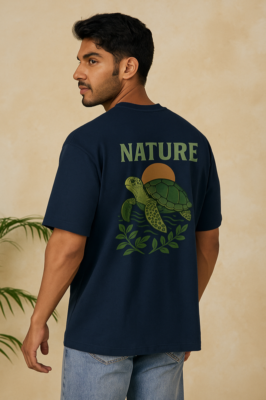 Man wearing a navy blue t-shirt with a turtle graphic and 'NATURE' text on the back, standing against a beige wall.