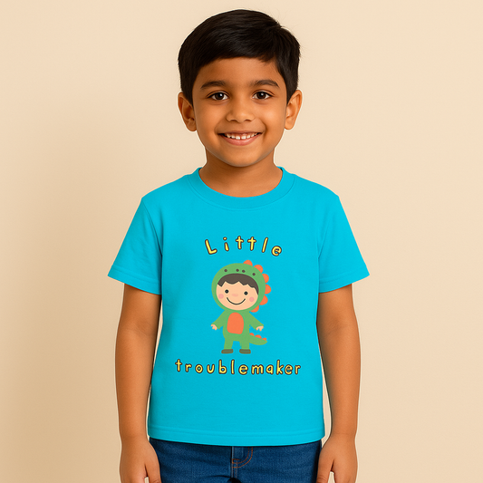  A digital photograph of a young Indian boy, around 8 years old, with fair skin tone, smiling and standing naturally. He is wearing a bright blue T-shirt with a cute “Little Troublemaker” design showing a cartoon child dressed in a green dinosaur costume. The look is completed with casual denim jeans, posed against a clean, neutral studio background with soft lighting, styled for an e-commerce clothing catalog.