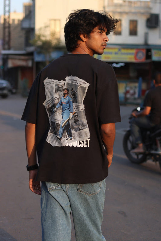 Person wearing a black t-shirt with a graphic design on the back, standing on a street.