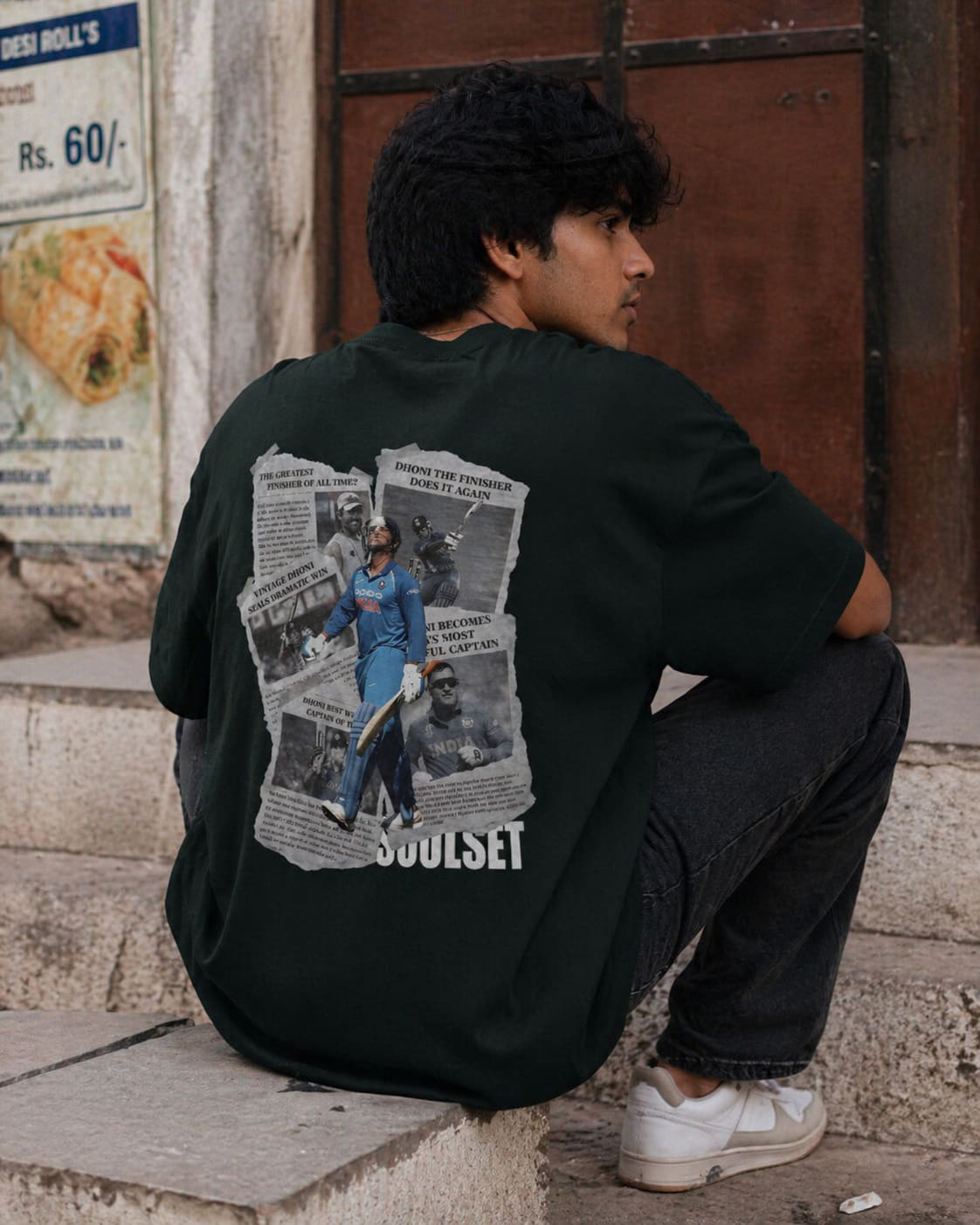 Person wearing a black hoodie with graphic designs and text, sitting on a step.