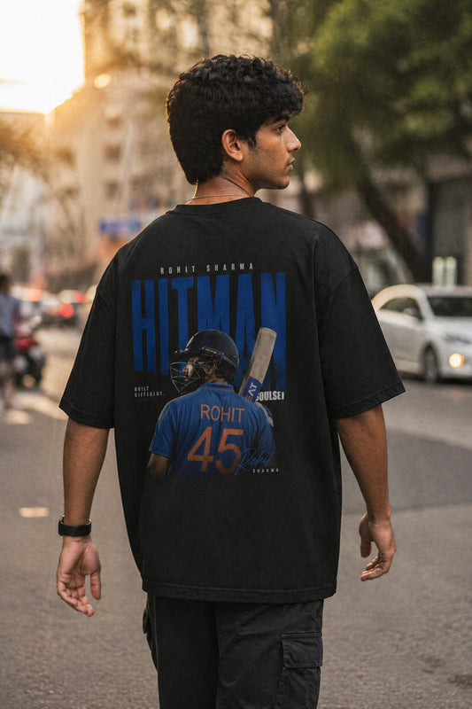 Person wearing a black t-shirt with a graphic of a baseball player and text on the back, standing on a street.