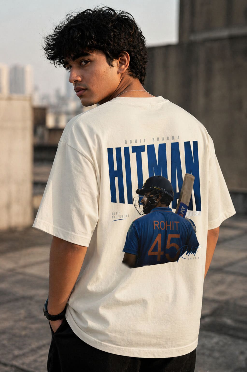 Person wearing a white t-shirt with 'HITMAN' and a graphic of a person in a blue shirt on the back, standing outdoors.