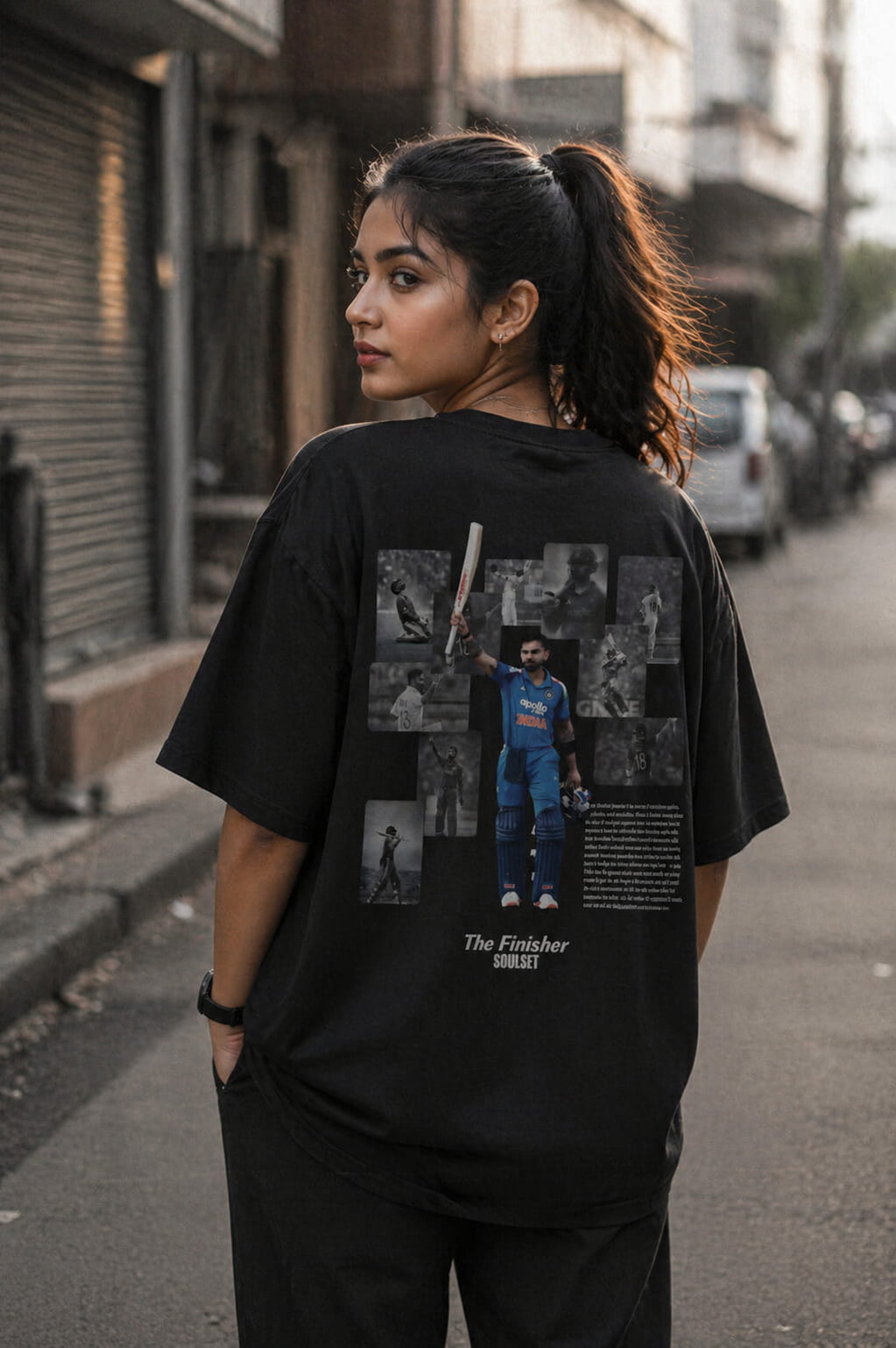 Person wearing a black t-shirt with a graphic design on the back, standing on a street.