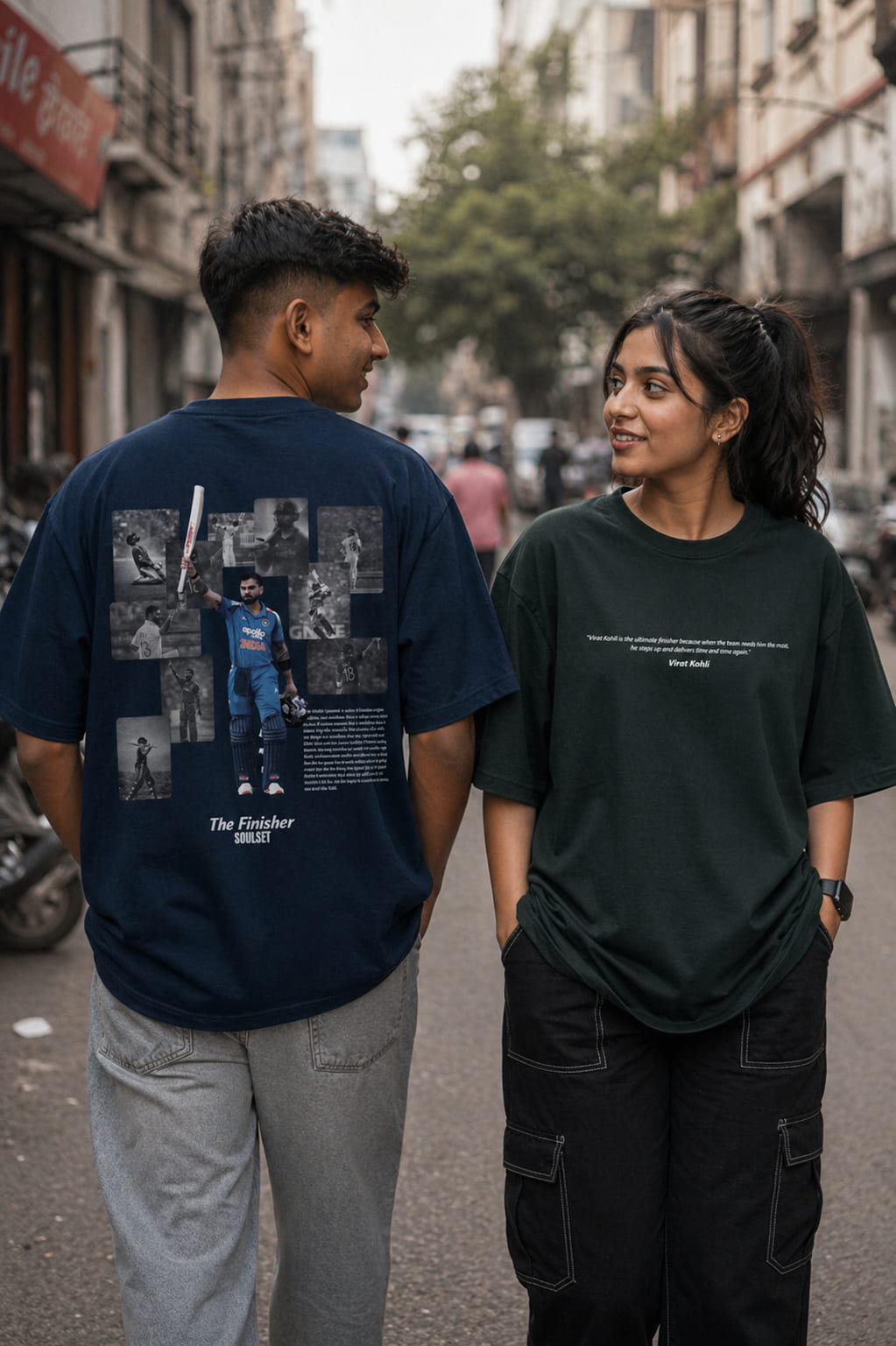 Two people standing on a street, one wearing a dark blue t-shirt with graphic designs and the other wearing a black t-shirt.