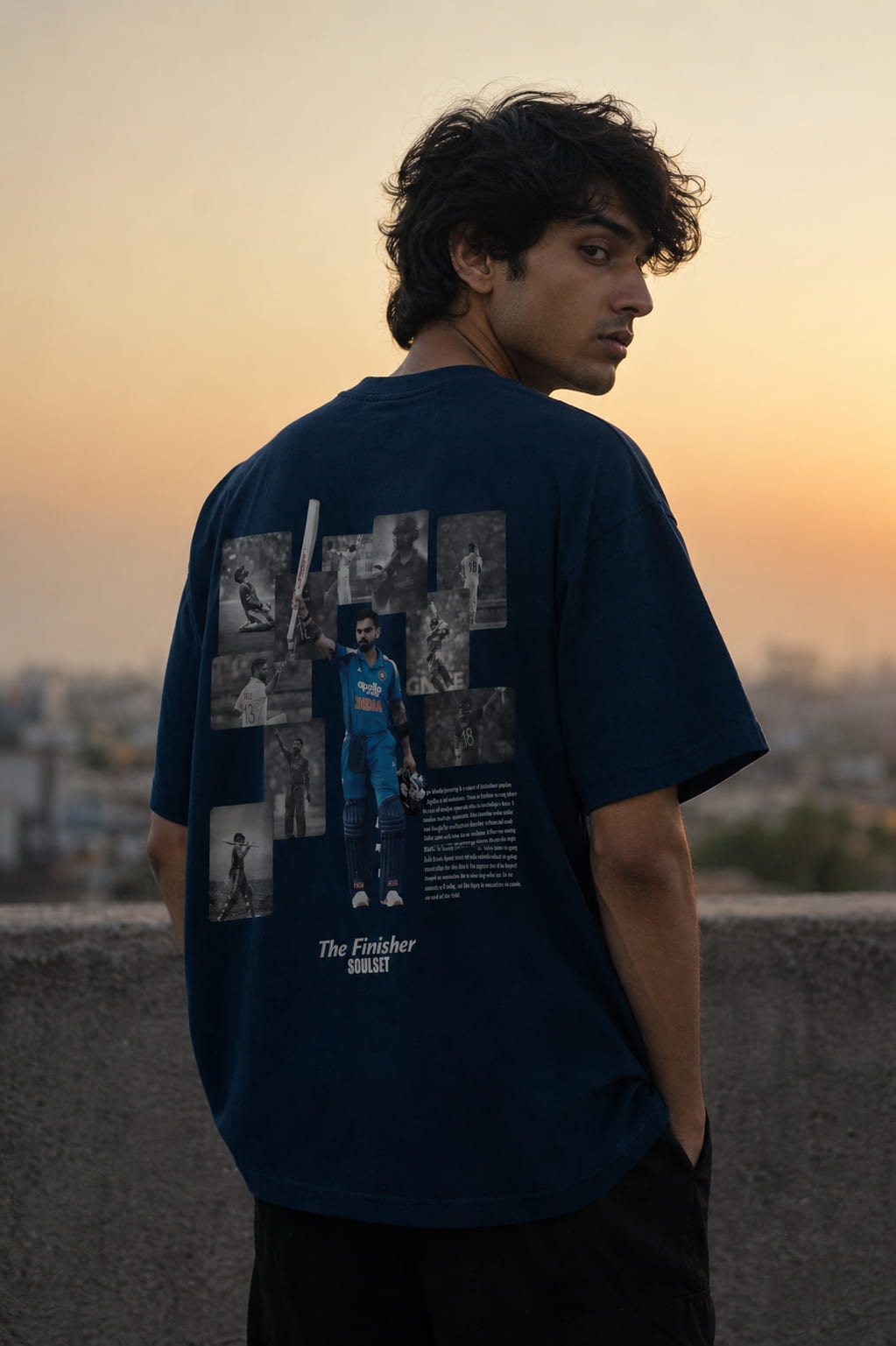 Person wearing a navy blue t-shirt with graphic designs, standing against a sunset cityscape.