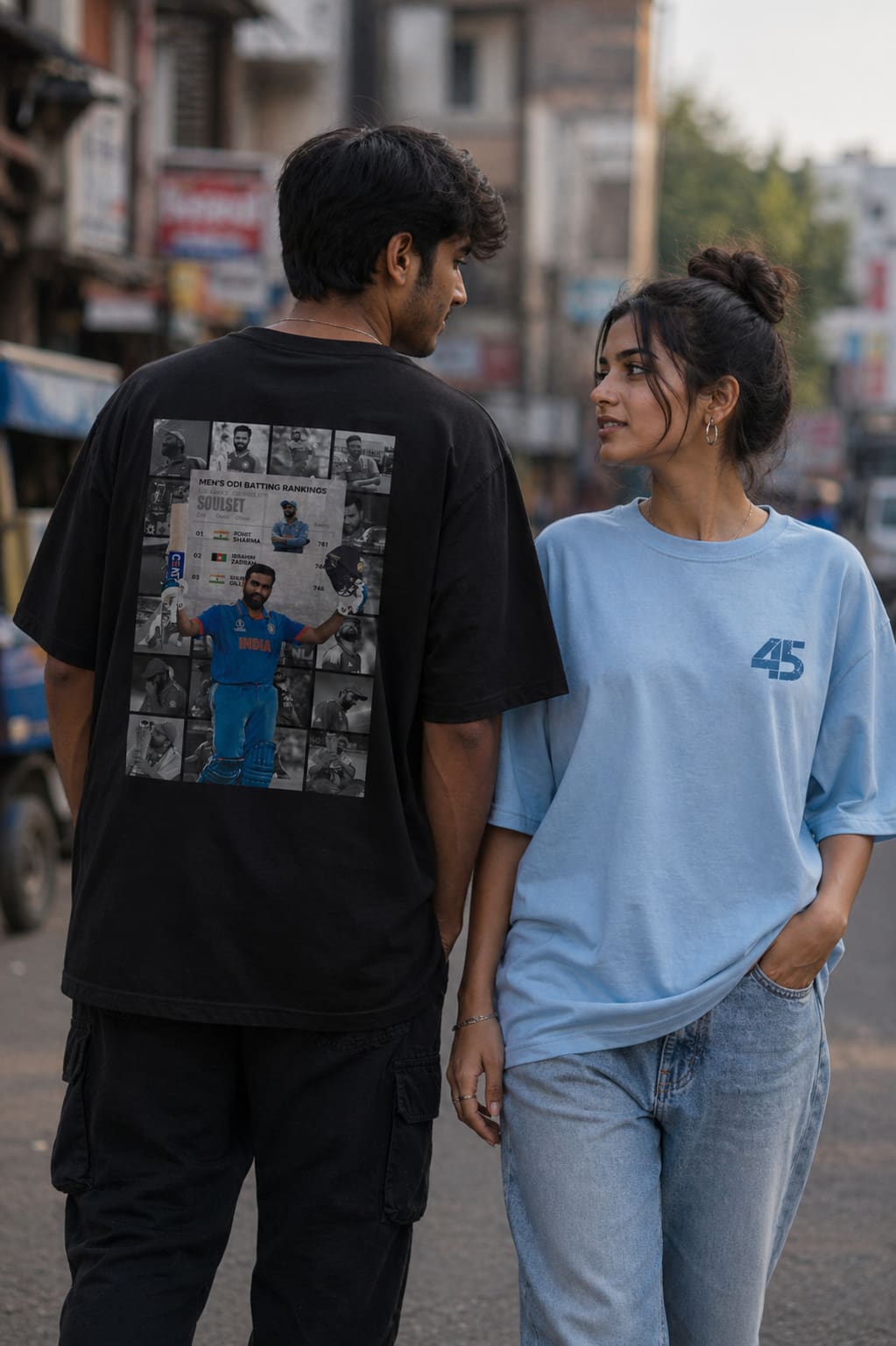 Two people standing on a street, one wearing a black t-shirt with a graphic design and the other wearing a light blue t-shirt with the number 45.