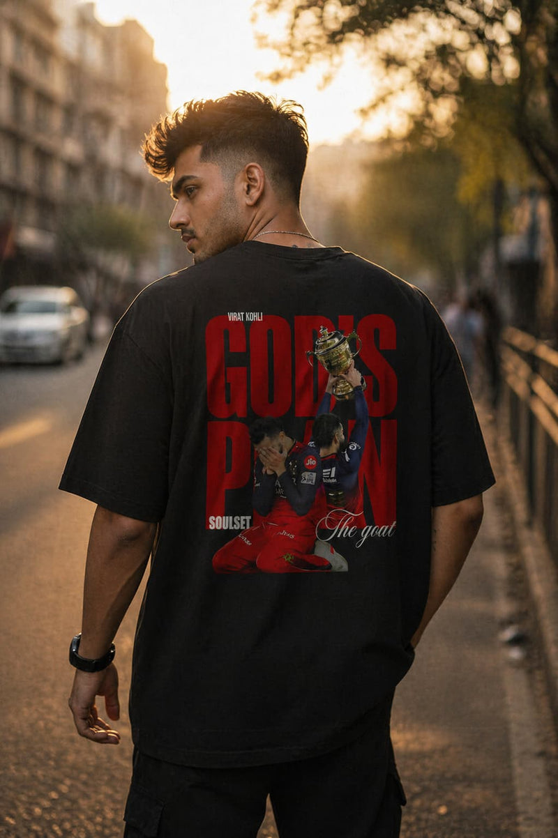 Man wearing a black t-shirt with red graphics VIRAT KOHLI GODS PLAN  and text on a street.