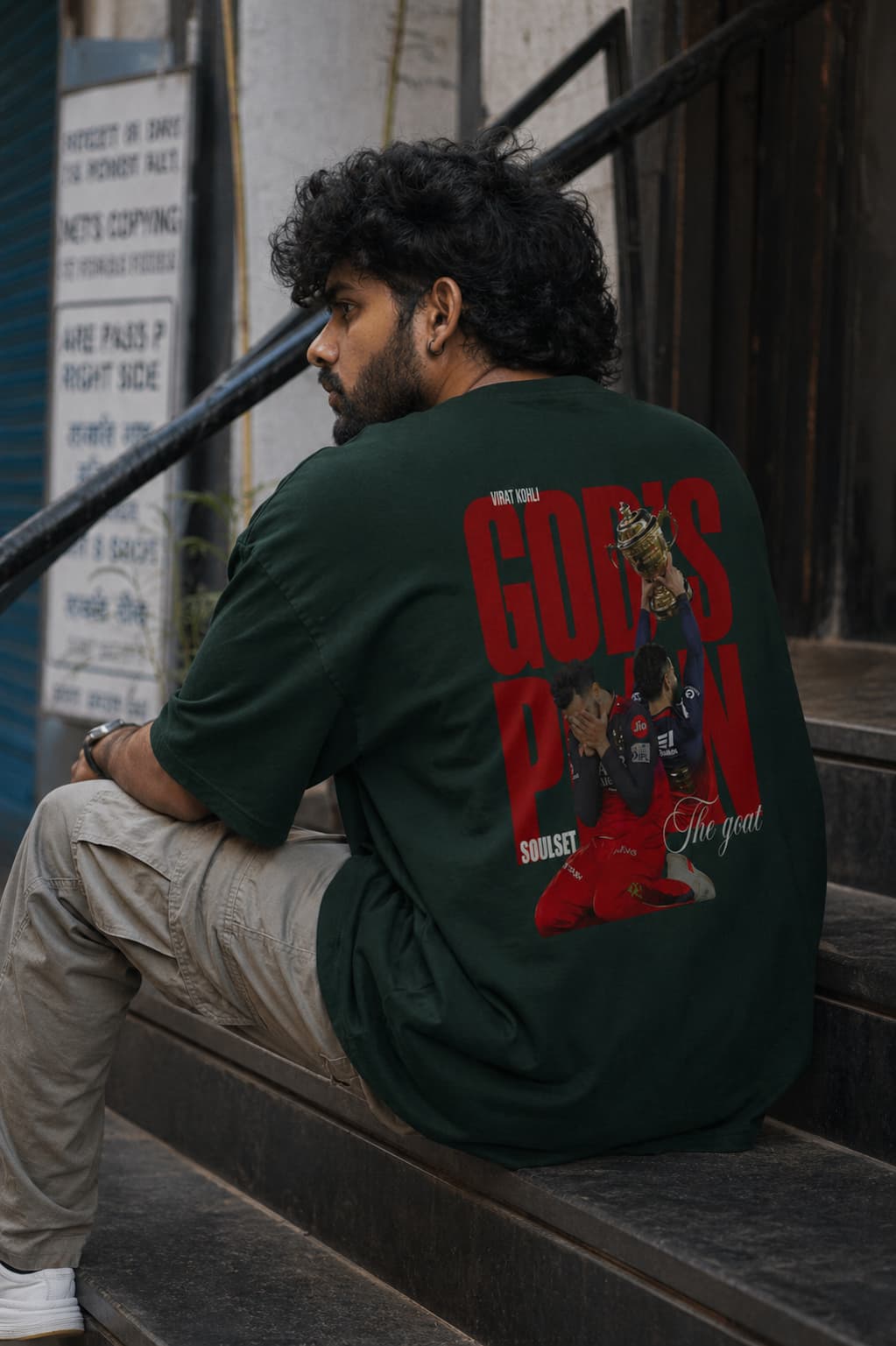 Man wearing a green t-shirt with graphic design sitting on steps.