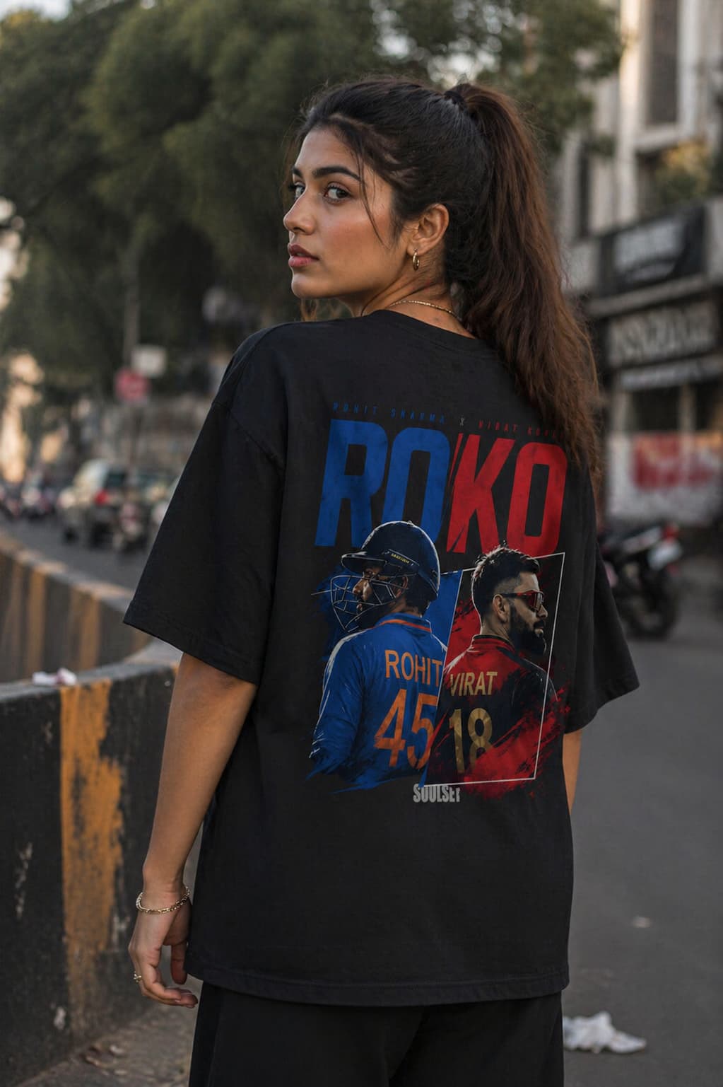 Woman wearing a black t-shirt with a graphic design and text on the back, standing on a street.