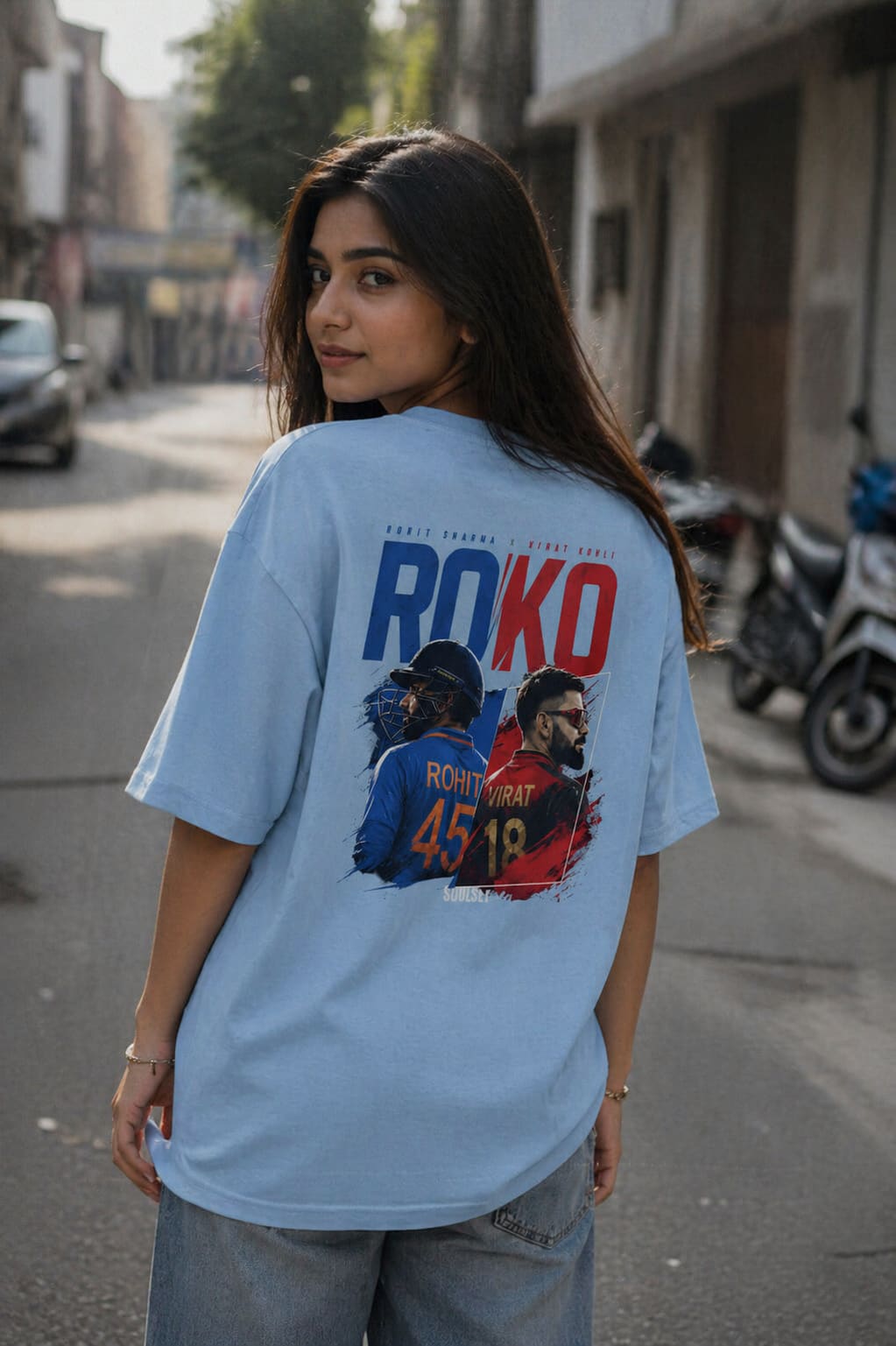 Woman wearing a light blue t-shirt with graphic designs and text on a street.