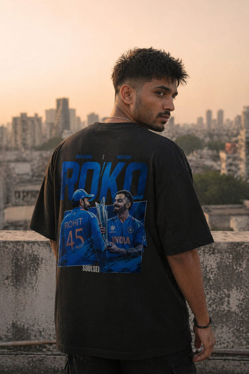 Person wearing a black t-shirt with graphics and text, standing on a rooftop with a cityscape in the background.