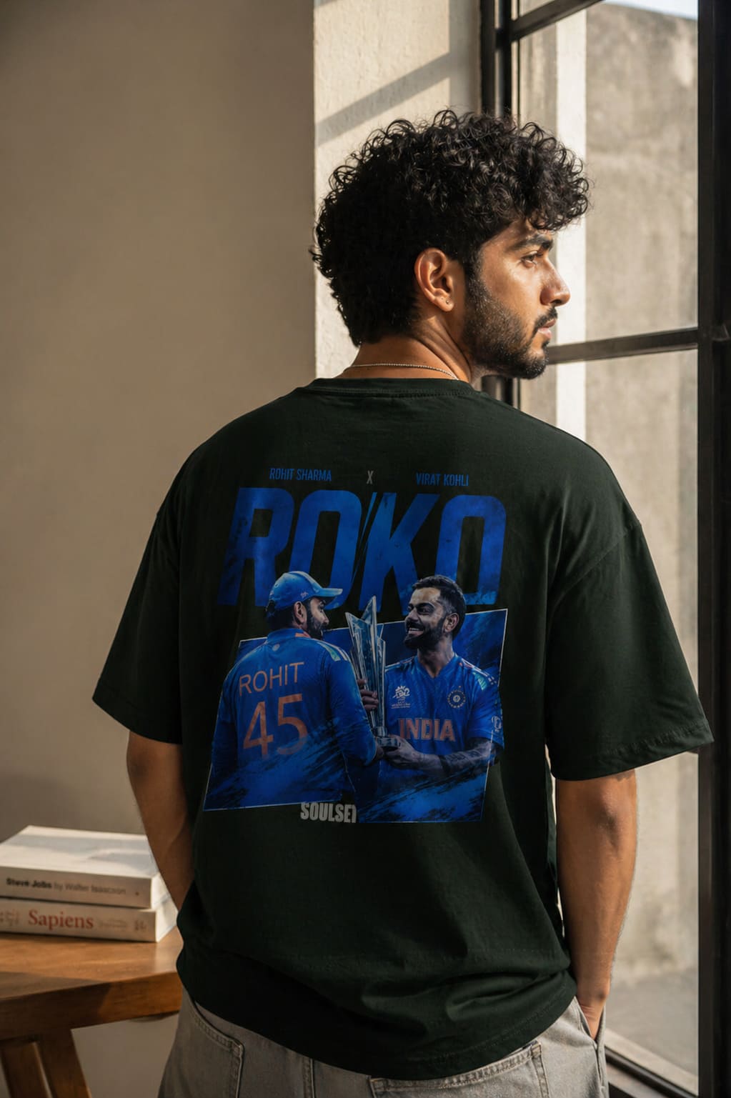 Person wearing a black t-shirt with blue graphics and text, standing indoors.