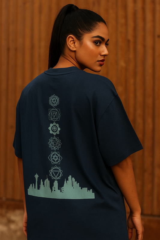 Indian female model wearing a navy blue oversized t-shirt with a bold back graphic featuring chakra symbols above a city skyline. The fit is modern and relaxed, with the model standing confidently facing the camera, showcasing the detailed back design. Perfect for streetwear and urban fashion.
