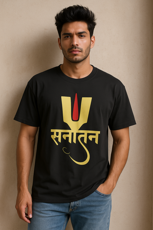 "A confident young Indian man wearing a black oversized T-shirt with a golden-yellow and red 'Sanatan' design in Devanagari script, standing against a beige wall with one hand in his pocket