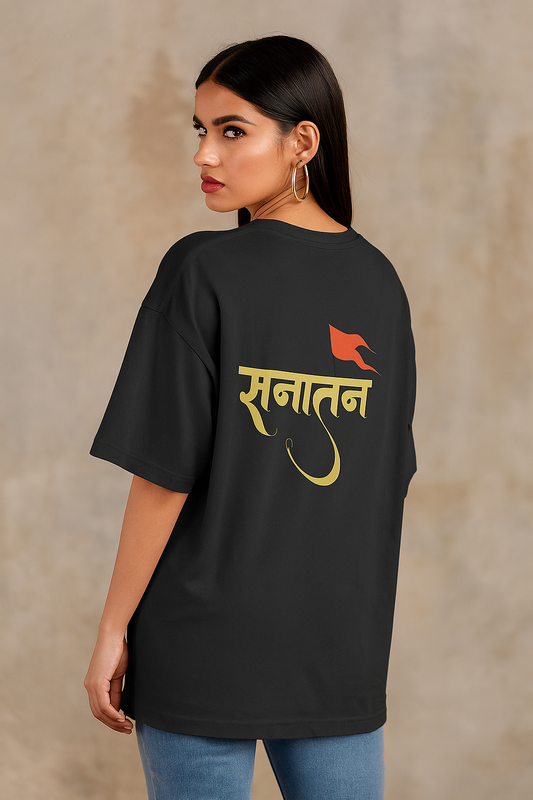 A confident young South Asian female model with fair skin and a fit build wearing a black oversized T-shirt with a bold 'Sanatan' text and saffron flag design on the back. She stands against a neutral beige background, looking over her shoulder with a stylish and bold expression, exuding elegance and confidence