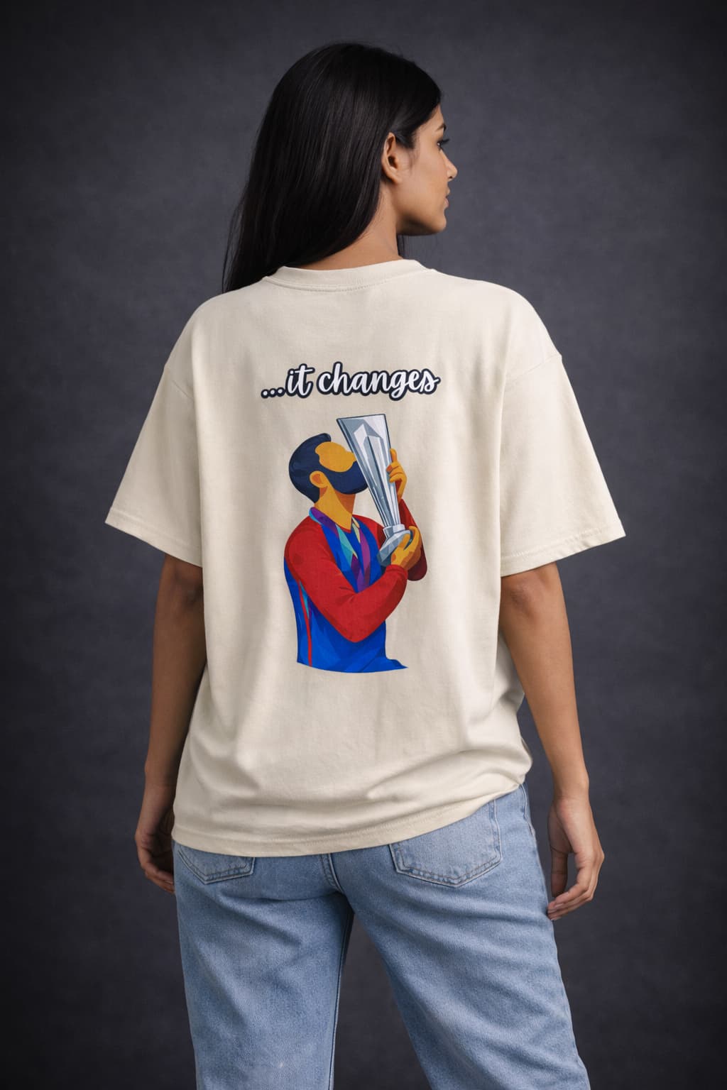 Person wearing a cream t-shirt with a graphic and text on the back, standing against a dark background.