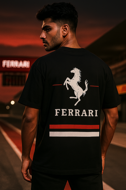 Indian  male model wearing a black Ferrari F1 t-shirt with vertical red and white racing stripes and Ferrari logo, standing confidently at a Formula 1 racetrack. Stylish, bold and modern apparel for F1 fans and streetwear lovers.