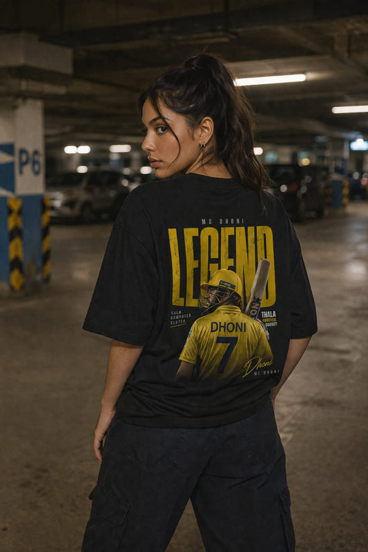 Person wearing a black t-shirt with a graphic DHONI and text in a parking garage.