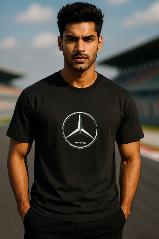A confident Indian male model with fair skin and a fit physique stands in a relaxed pose, facing away to showcase the FRONTof her black oversized Mercedes-AMG Petronas F1 Team t-shirt. The t-shirt features bold white and teal typography with “MERCEDES LOGO,” printed on it. The model is positioned on a Formula 1 pit lane at sunset, with a sleek Mercedes-Benz garage in the background, exuding a bold and stylish F1-themed atmosphere.
