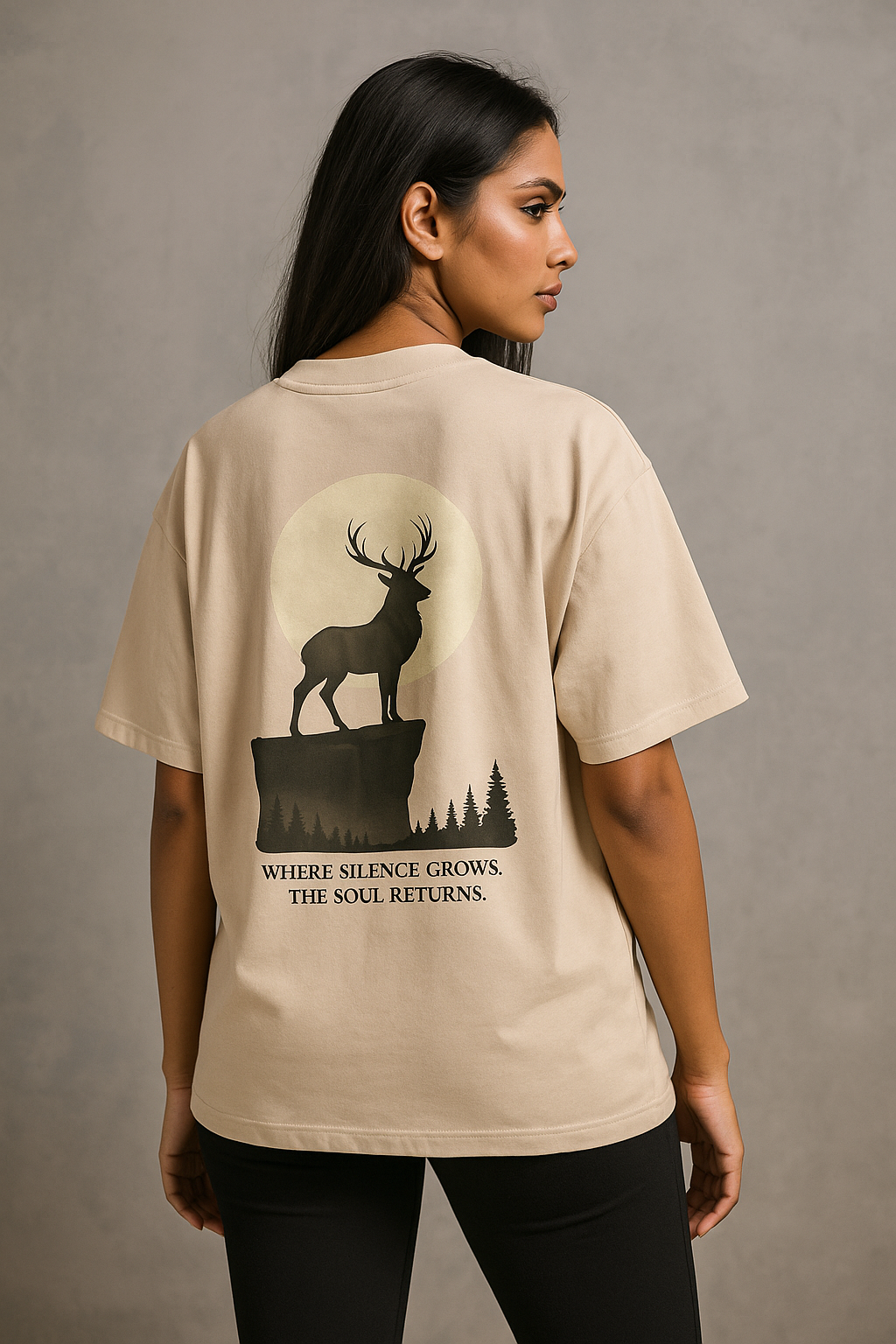 Woman wearing a beige t-shirt with a deer graphic and text on the back against a gray background