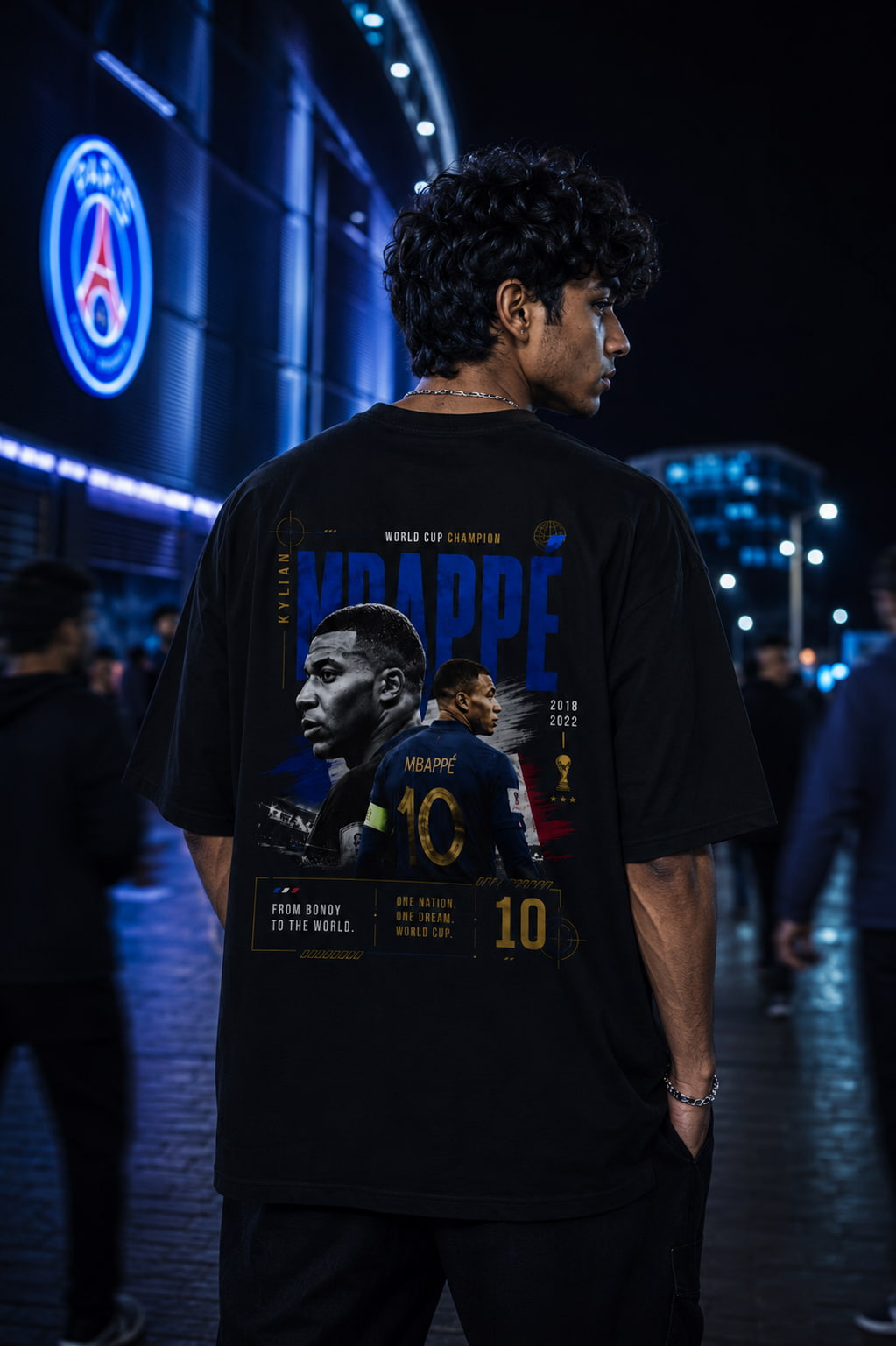Person wearing a black t-shirt with a graphic design of a football player, standing in front of a stadium at night.