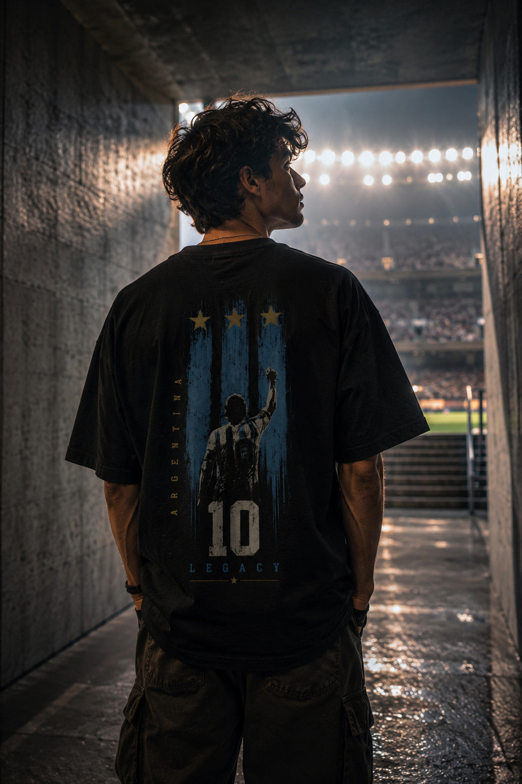 Person wearing a black t-shirt with a graphic design, standing in a tunnel with stadium lights in the background.