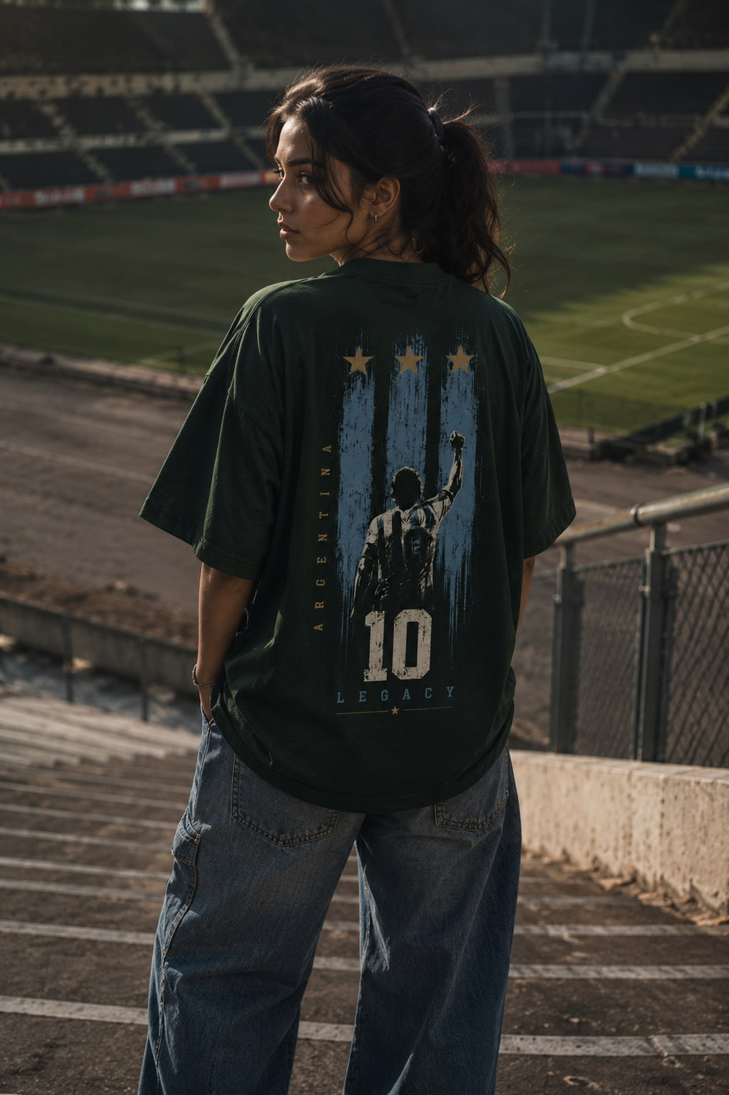 Person wearing a green t-shirt with a graphic design in an outdoor stadium setting