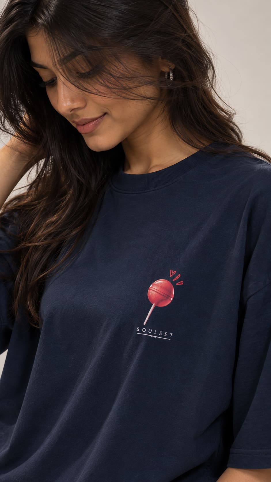 A woman wearing a navy blue oversized t-shirt with a small red and white graphic of a lollipop on the left chest, with the word 'SOULSET' printed below it.