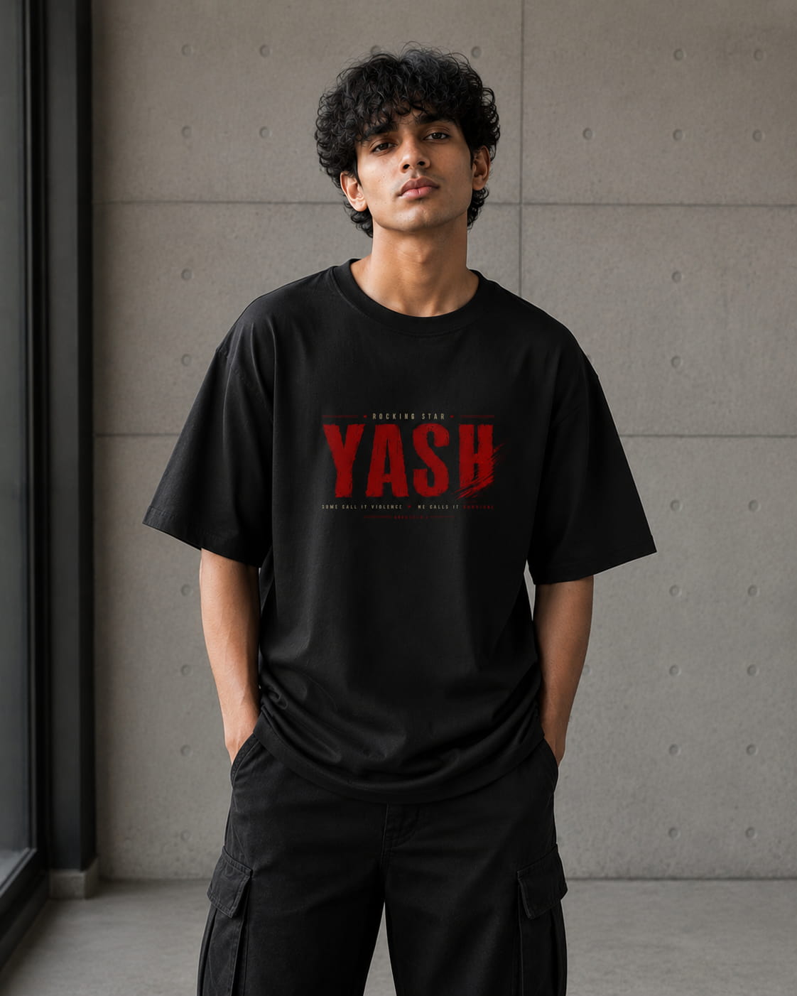 A man wearing a black crewneck t-shirt with a red distressed graphic reading 'YASH' on the chest, paired with black cargo pants, standing against a textured gray concrete wall.
