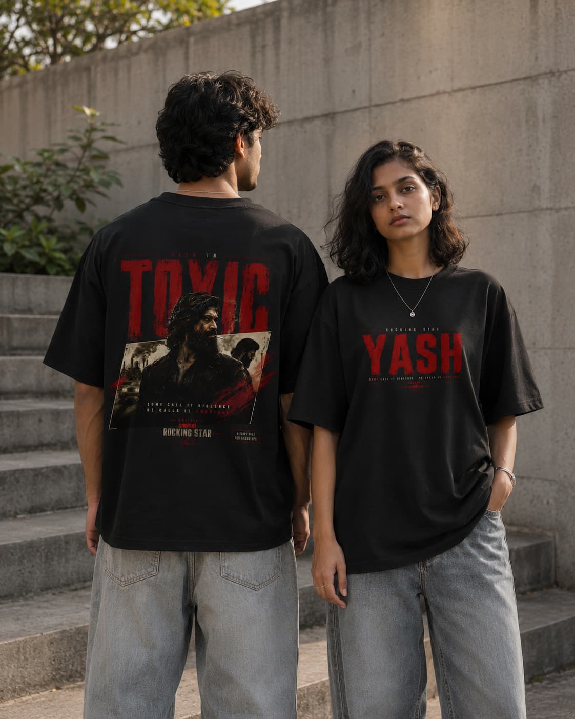 Two models wearing black graphic t-shirts in an outdoor concrete setting. The model on the left shows the back of the shirt with a large red 'TOXIC' graphic and character print, while the model on the right shows the front of the shirt with the name 'YASH' in red.