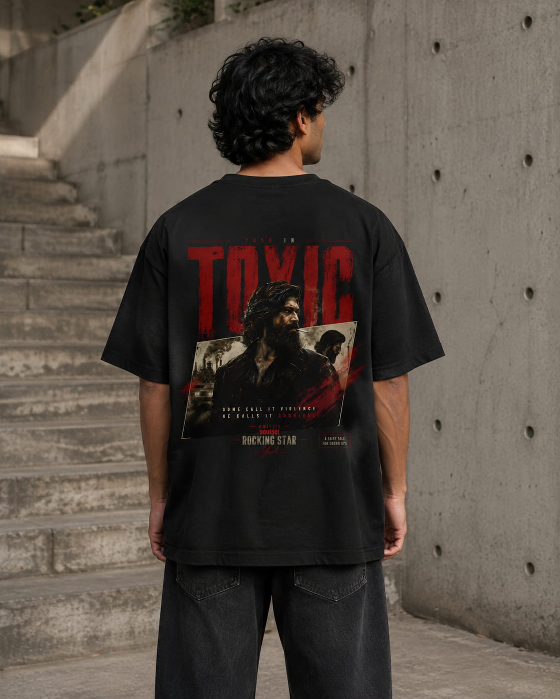 A man viewed from behind wearing a black graphic t-shirt with a large red and white print on the back, standing in front of a concrete wall and staircase.