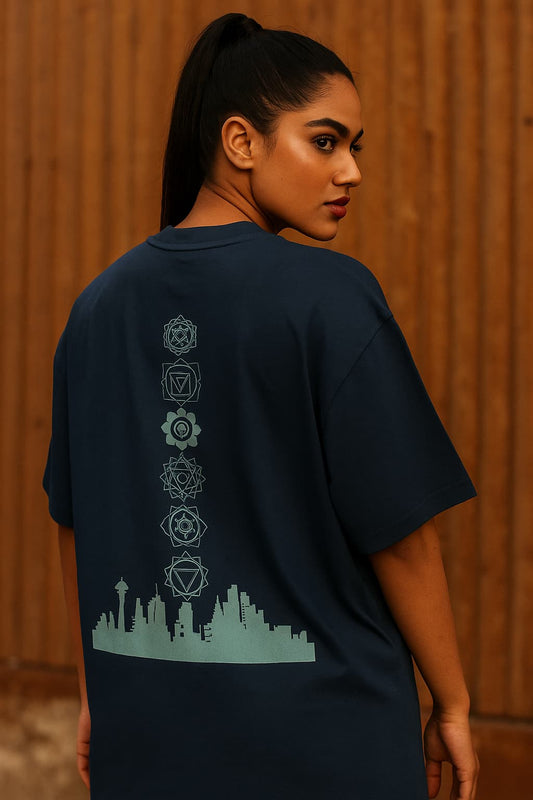 Person wearing a navy blue t-shirt with a cityscape design on the back against a wooden wall.